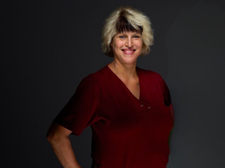 Vanessa Berlin, Frau von Roland Berlin leitet den Wellnessbereich königSPA Physiotherapeutin Vanessa Berlin lächelt bei einem Portraitfoto vor dunklem Hintergrund.