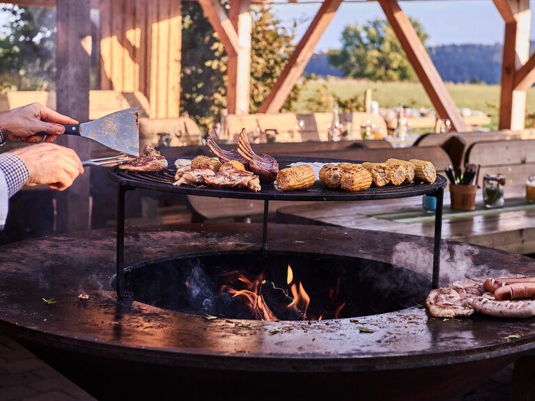 Für Feierlichkeiten sind die GiganTische unterm Biberschwanzdächle besonders geeignet. Verschiedene Stückchen Fleisch sowie Maiskolben werden auf dem großen Grill im Wanderheim Zavelstein gegrillt.