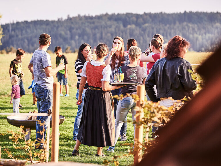 Eine junge Servicemitarbeiterin hält ein Tablett mit Sektgläsern in der Hand und verteilt sie an die herumstehenden Gäste