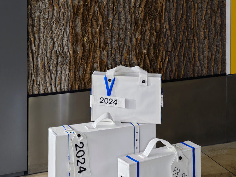 3 weiße Koffer mi blauen Bändern die ein Etikett mit dem Jahr 2024 haben.