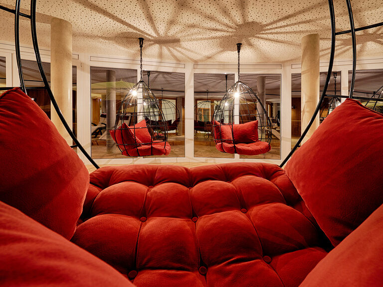 Three hanging chairs with red pillows at night.