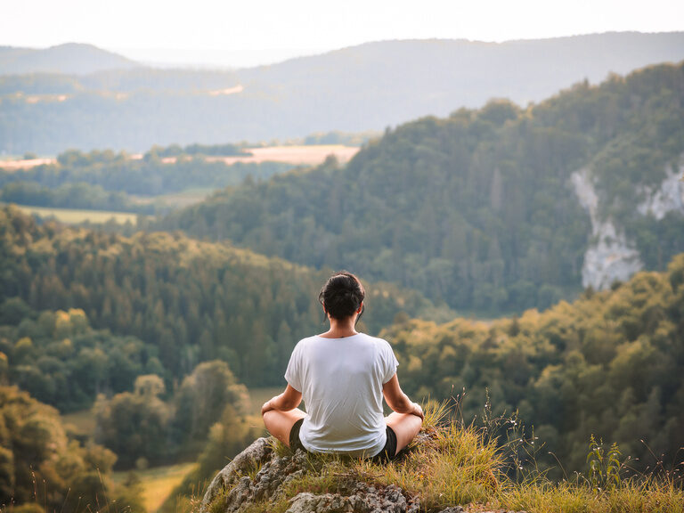 Auf einem Felsen mit Blick in die Tiefen des Schwarzwalds meditiert eine Frau in Ruhe und Gelassenheit.
