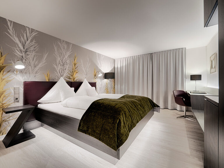 Die Zimmerkategorie Teinachtal im Haupthaus Hotel Lamm besticht durch modernen Einrichtungsstil. Doppelbett und Schreibtisch in einem modernen und geräumigen Hotelzimmer mit zugezogenen Gardinen.